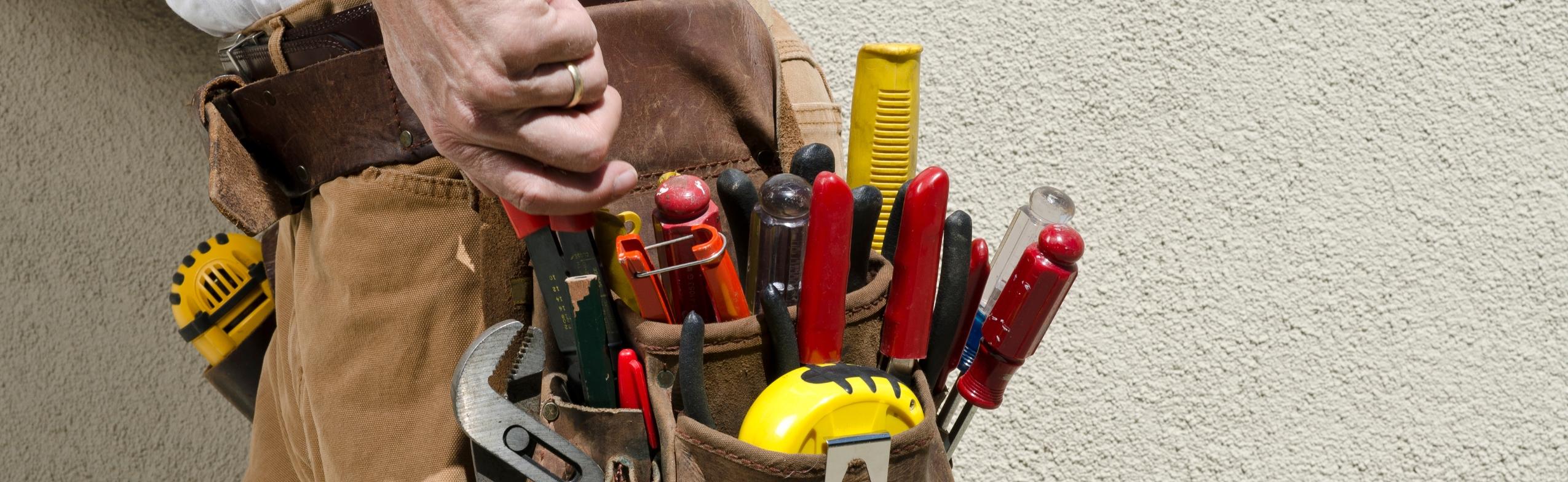 An electrician's tool pouch. It is full of tools including pliers, tape measure, and screw drivers.