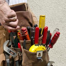 An electrician's tool pouch. It is full of tools including pliers, tape measure, and screw drivers.